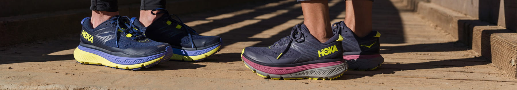 A close up of two people standing wearing HOKA shoes.