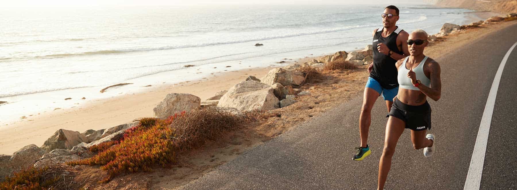 A man and a woman running down the side of the road, oceanside.